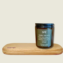 Candle jar labeled 'SPè Dark Nights' on a wooden stand with a beige background
