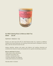 A product listing card for Go Wild Calming Rose & Hibiscus Bath Tea. The image features a clear glass jar containing a light-colored herbal tea blend with a pink label and a gold lid, set against a solid pale beige background.